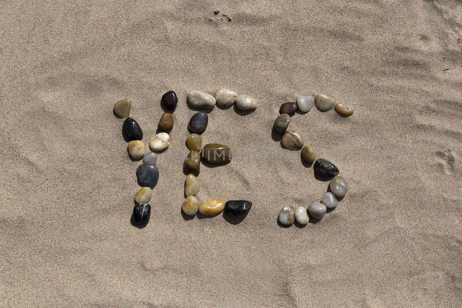 A set of pebbles in a sandy beach forming the word yes