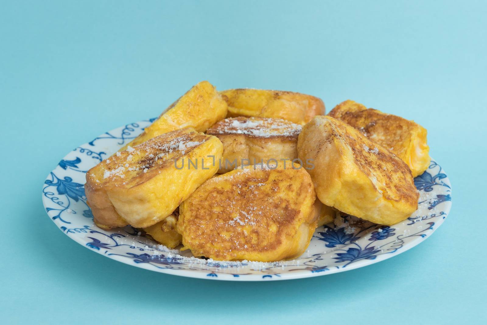A plate of French toast on a white and blue floral designed plate on a light blue background.