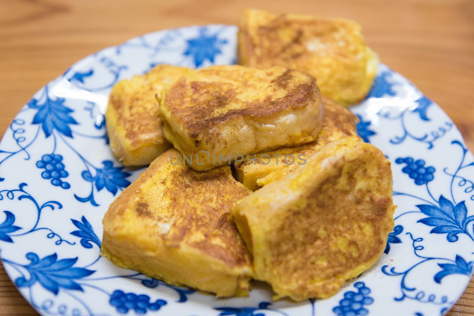 A plate of French toast on a white and blue floral designed plate on a wooden table background.