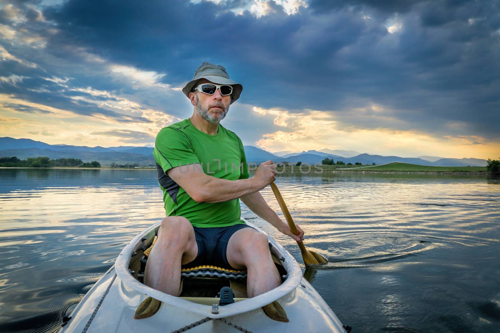 senior male paddling an expedition canoe on lake at dusk with Front Range of Rocky Mountains in background