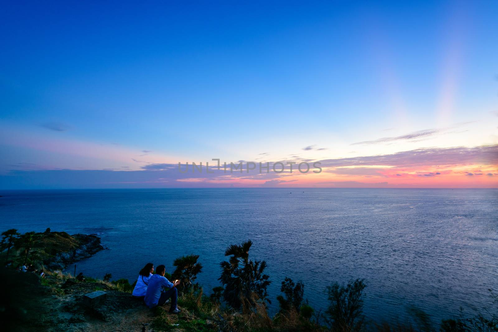 PHUKET, THAILAND - APRIL 28 2015: Couple and tourists taking photos and waiting for the sunset over the sea on Laem Phromthep Cape scenic point is a famous attractions of Phuket Province, APRIL 28 2015 in Thailand
