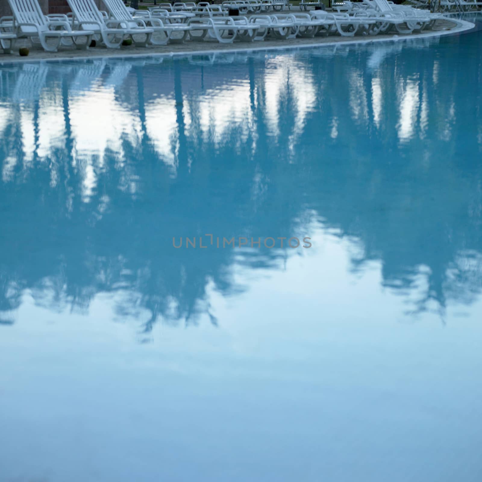 White plastic chairs in a row around a resort pool in the tropics