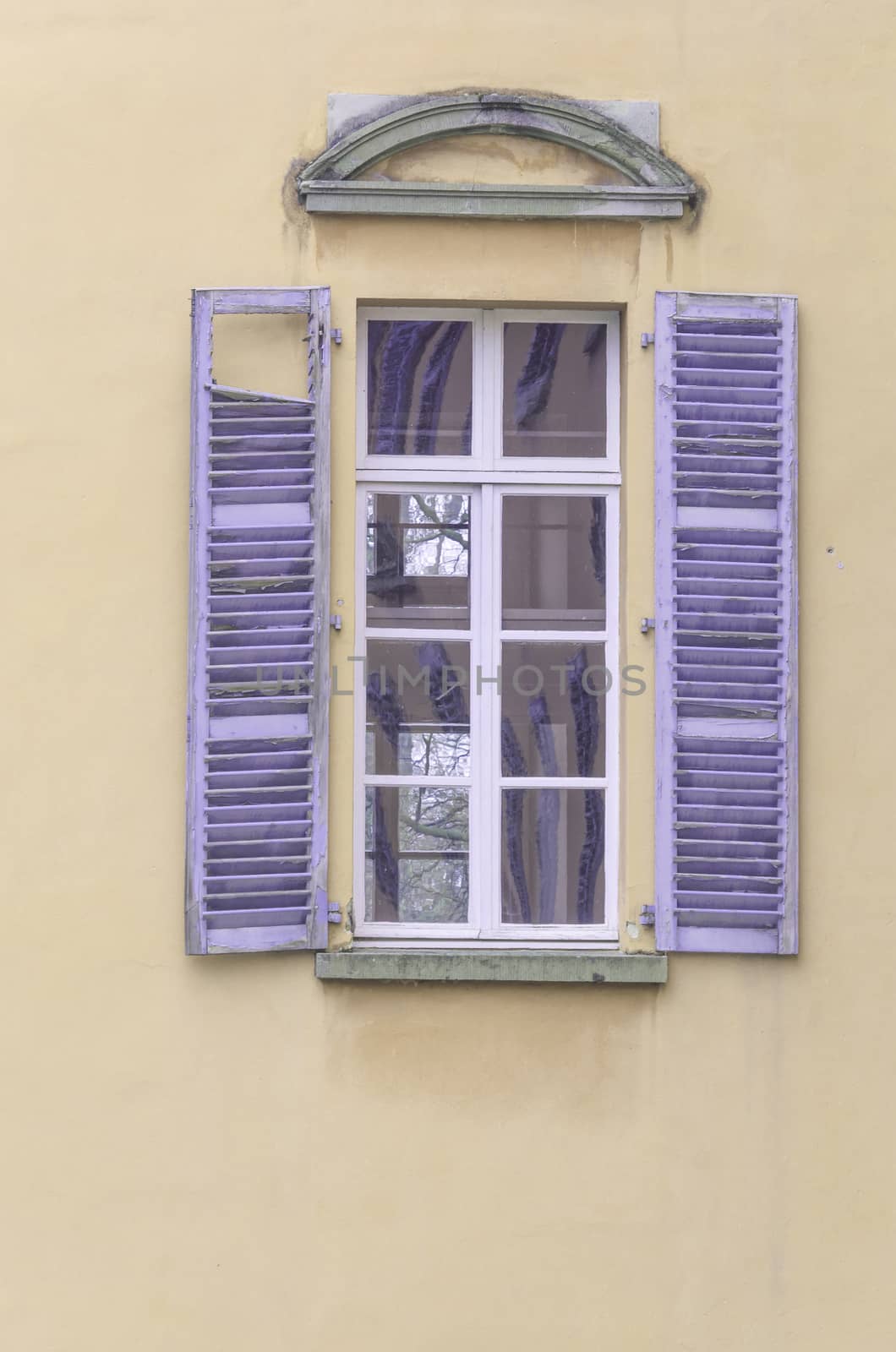 Old window with purple wooden shutters on a beige facade.
