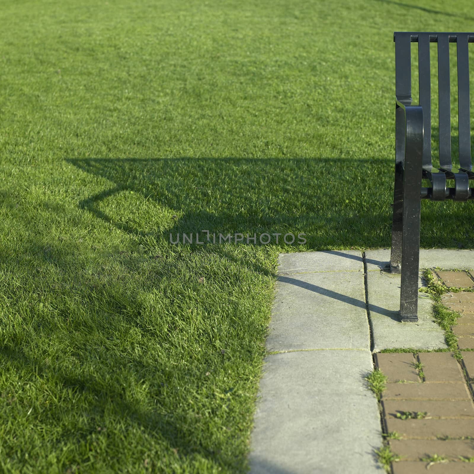 Black metal park bench near a brick path and perfect green grass