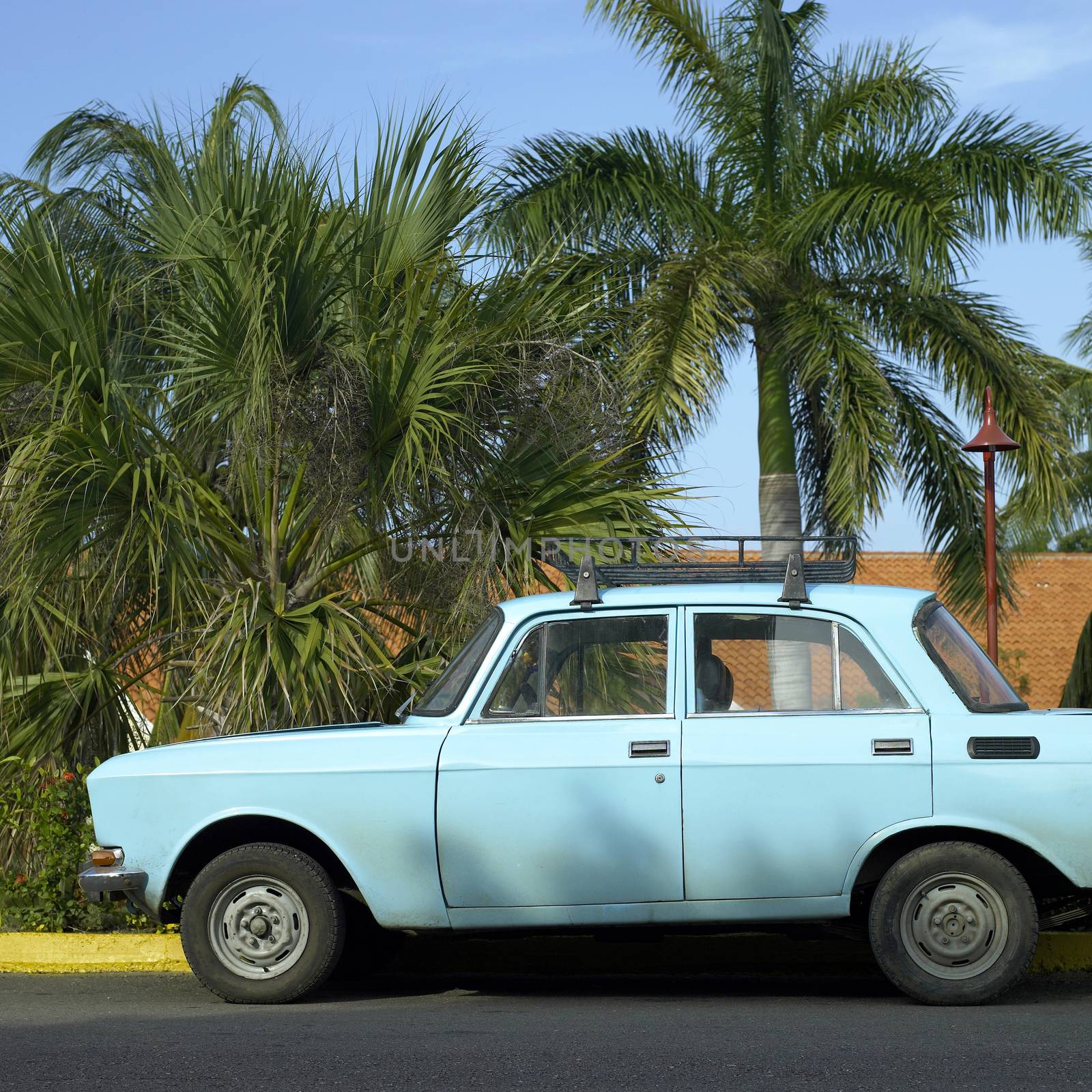 Cute vintage blue car near the yard of a house in a tropical location