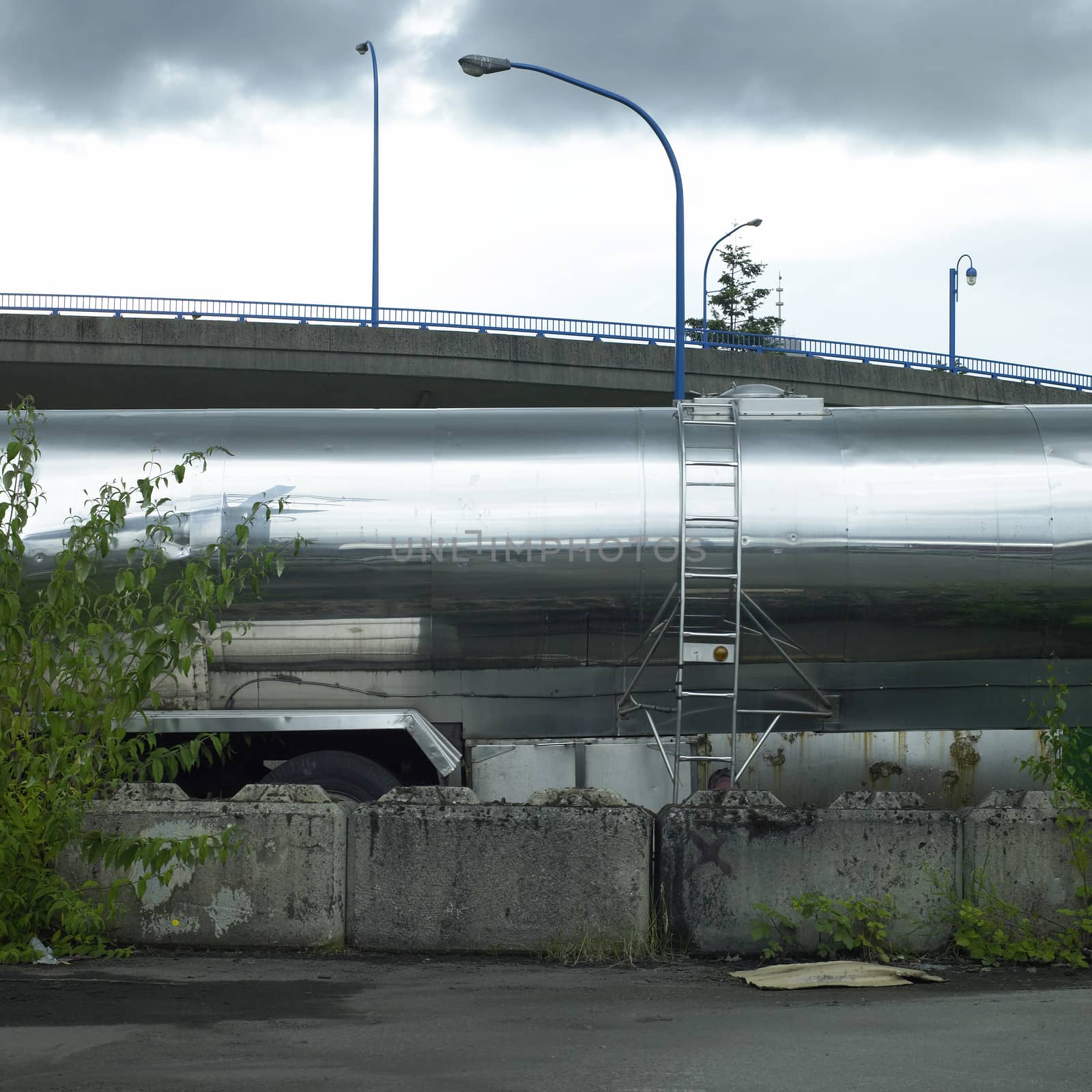 Shiny chrome tanker trailer with side ladder parked near a bridge
