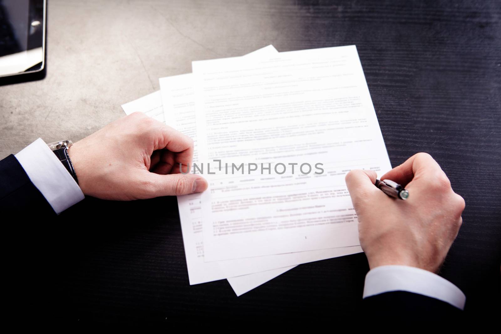 Image of human hand with pen over documents at workplace.