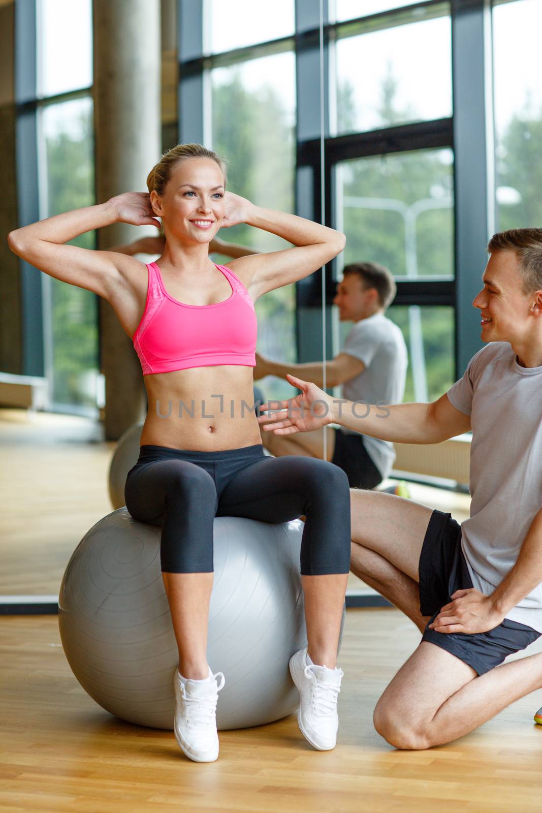 smiling man and woman with exercise ball in gym by dolgachov