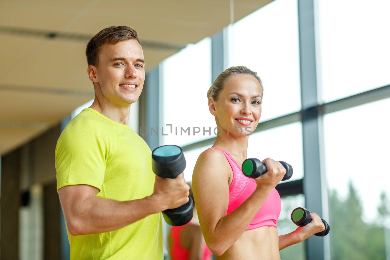 sport, fitness, lifestyle and people concept - smiling man and woman with dumbbells exercising in gym