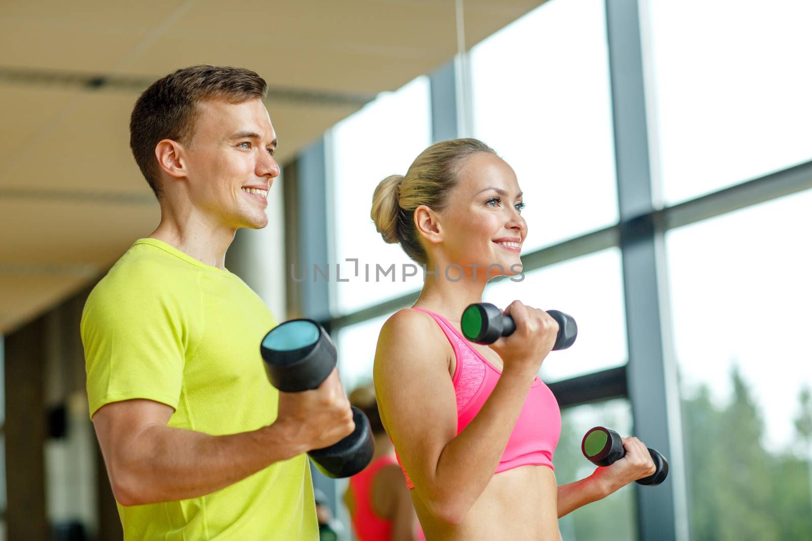 sport, fitness, lifestyle and people concept - smiling man and woman with dumbbells exercising in gym