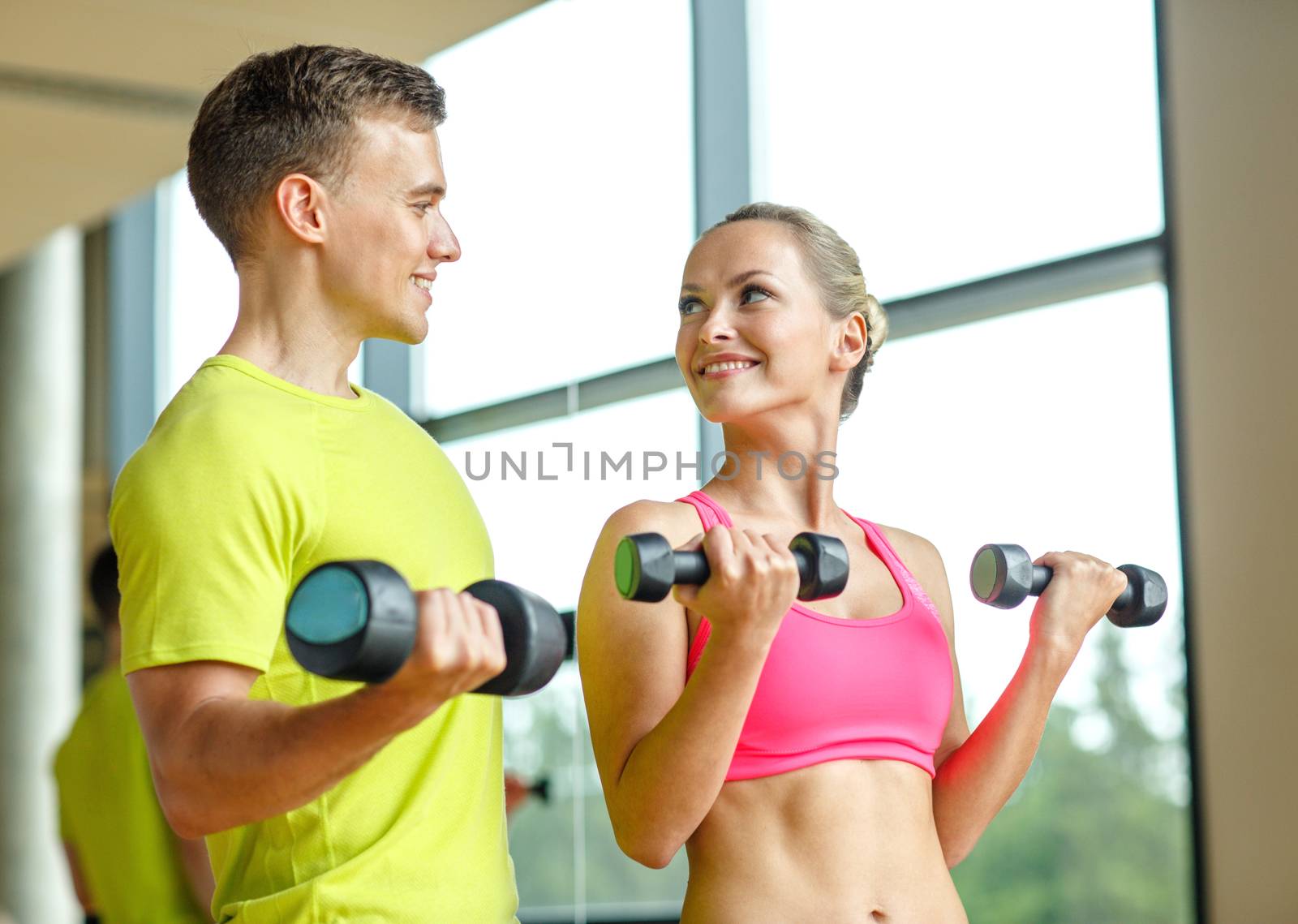 smiling man and woman with dumbbells in gym by dolgachov