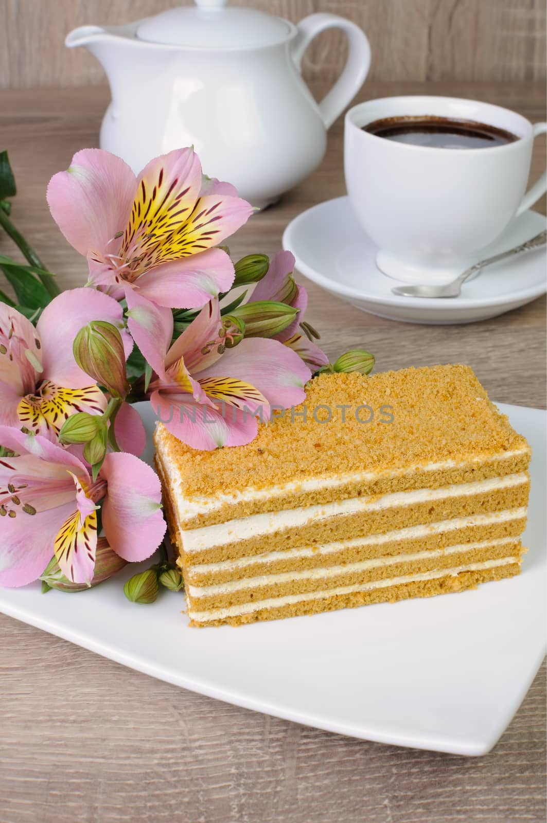 Piece of honey cake with a cup of coffee on a table with a flower