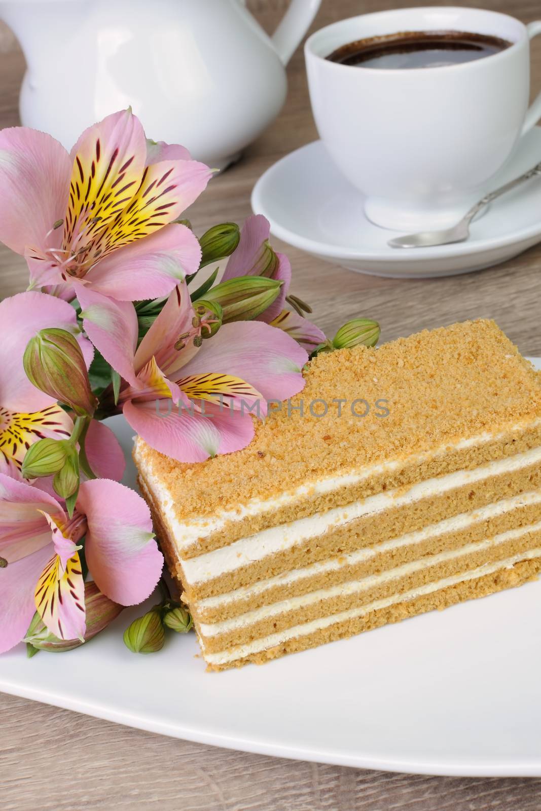 Piece of honey cake with a cup of coffee on a table with a flower