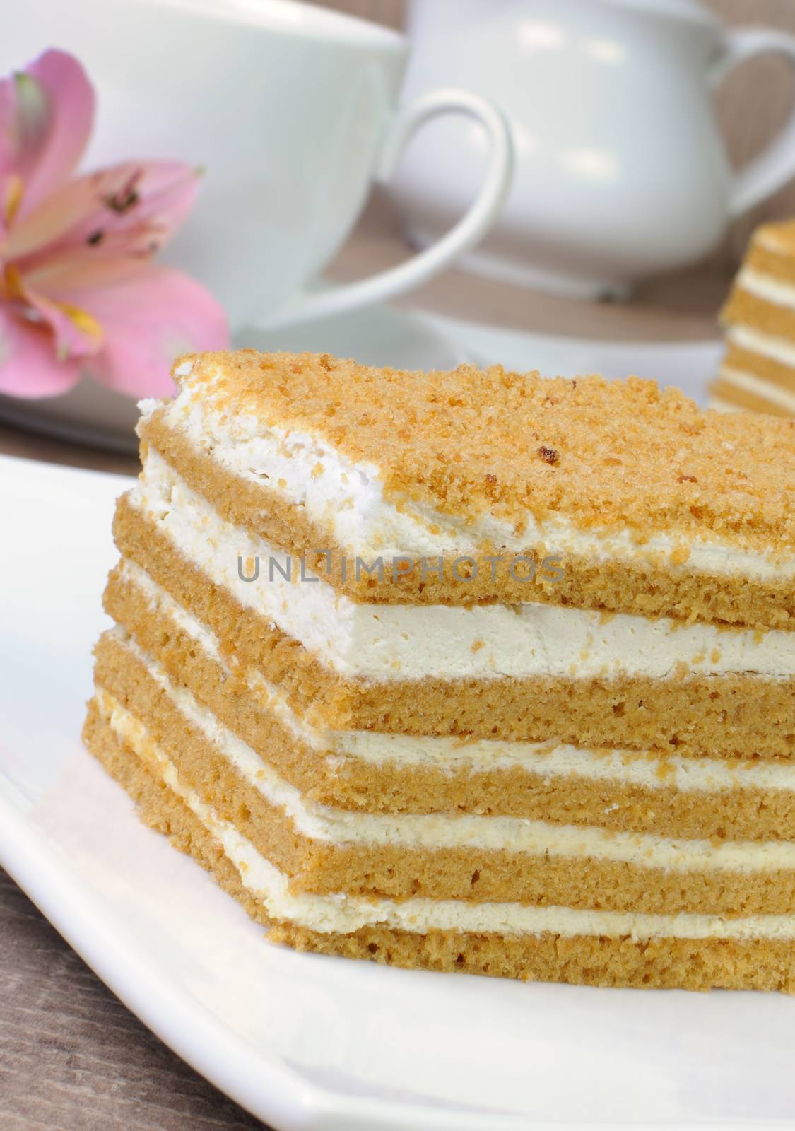 Piece of honey cake with a cup of coffee on a table with a flower