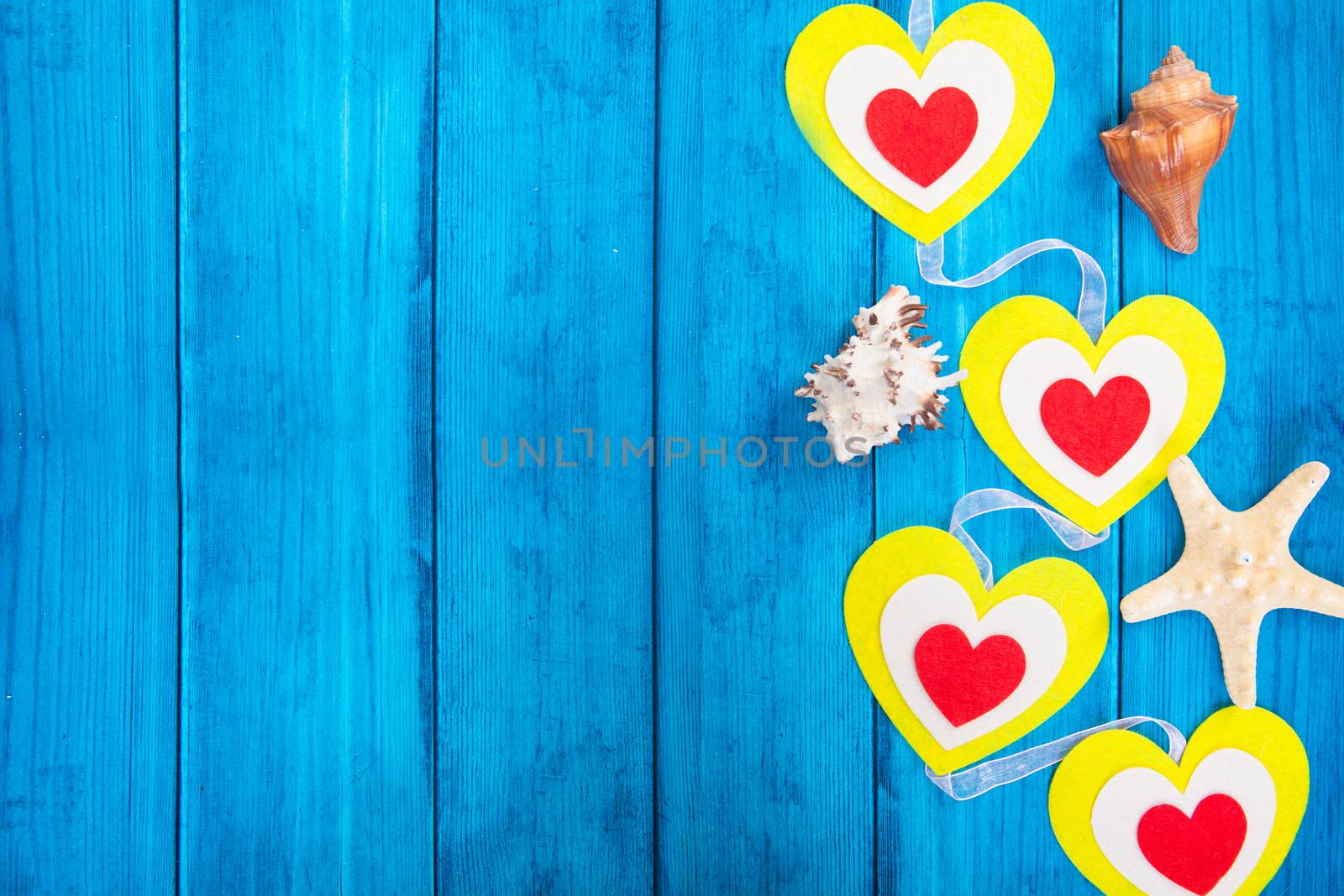 red hearts on a colored rope and starfish on blue wooden background by traza