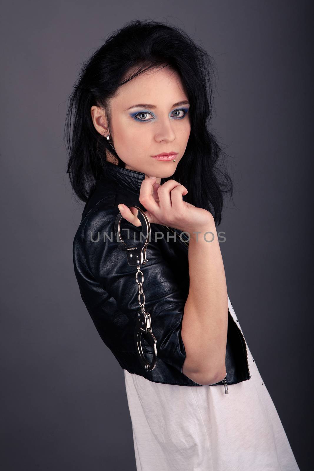 pretty girl in leather jacket with police handcuffs on a gray background