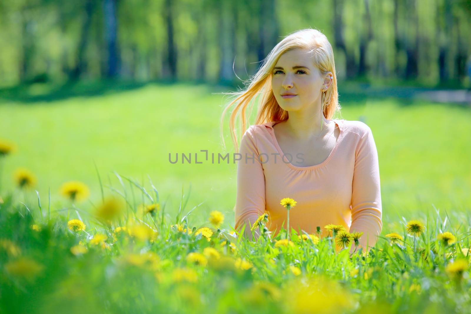 Beautiful young woman laying in spring park with dandelion flowers