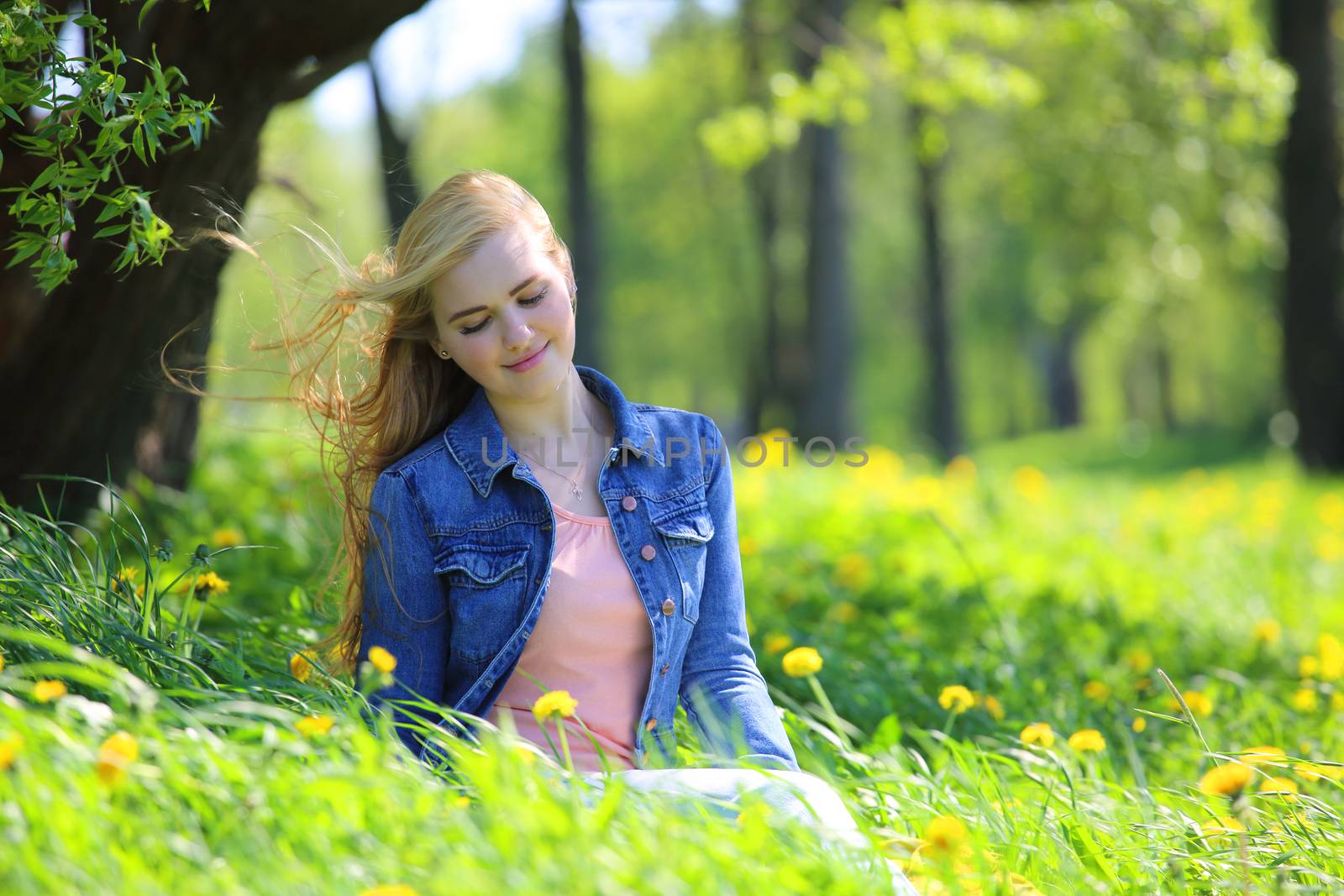 Beautiful young woman sitting in spring park with dandelion flowers
