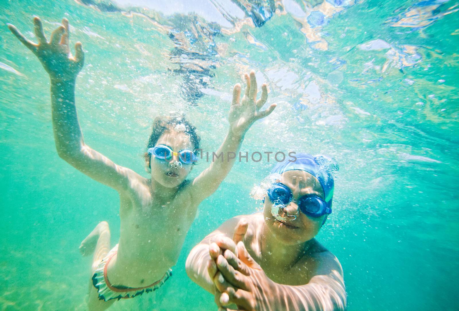 Two kids - boy and a girl, about seven years old are swimming underwater in a sea or ocean.
