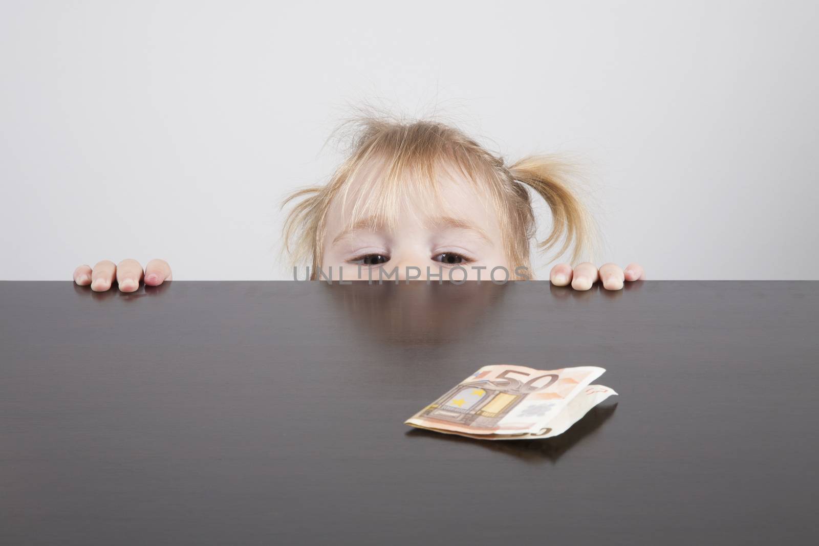 portrait of blonde caucasian baby nineteen month age with pigtails chubby face  looking at Euro banknote on brown table horizontal