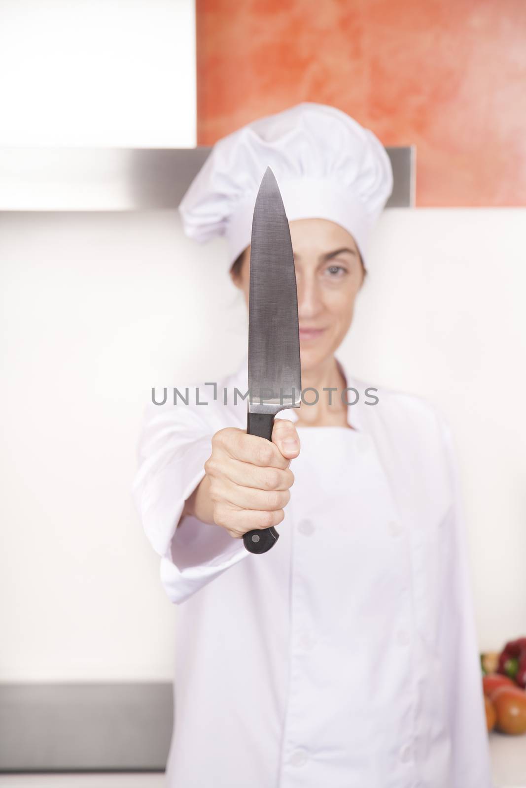 big kitchen knife in right hand of brunette happy chef woman with professional jacket and hat  white and orange kitchen