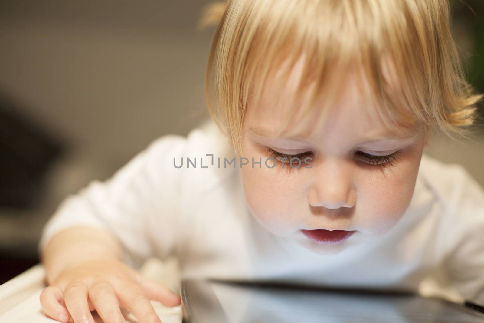 blonde nineteen month age baby white sweater looking at close digital tablet inside home