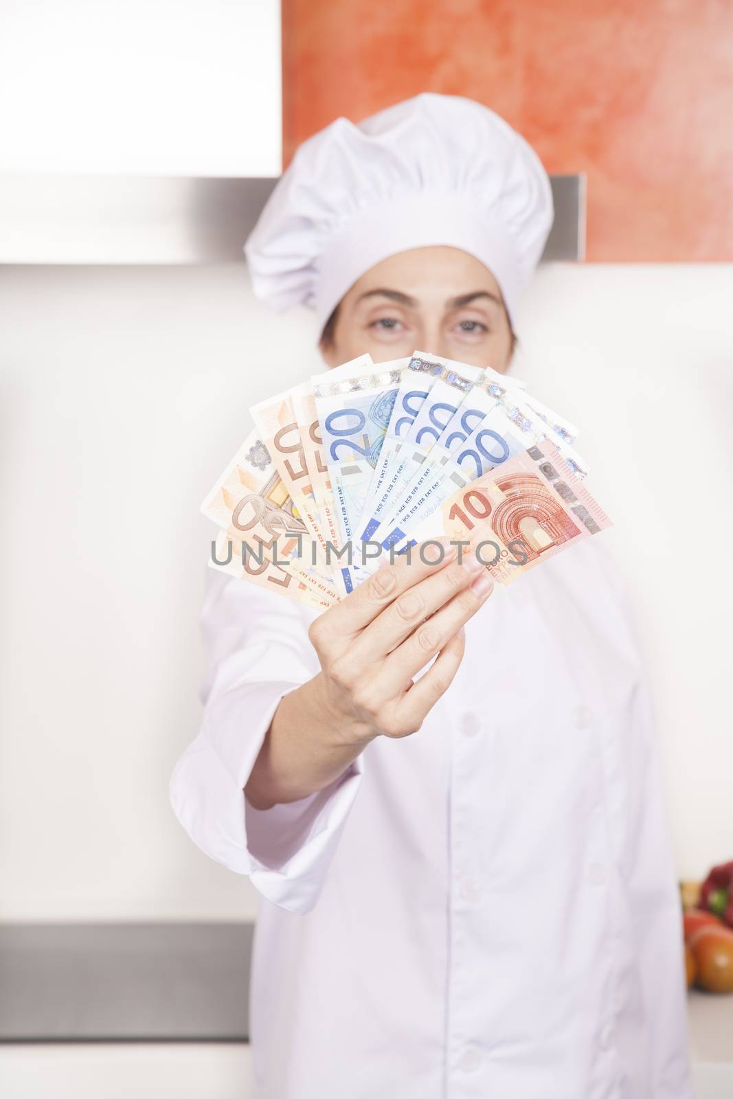 wad of fifty twenty and ten Euro banknotes wad in hands of brunette happy chef woman with professional jacket and hat in white and orange kitchen