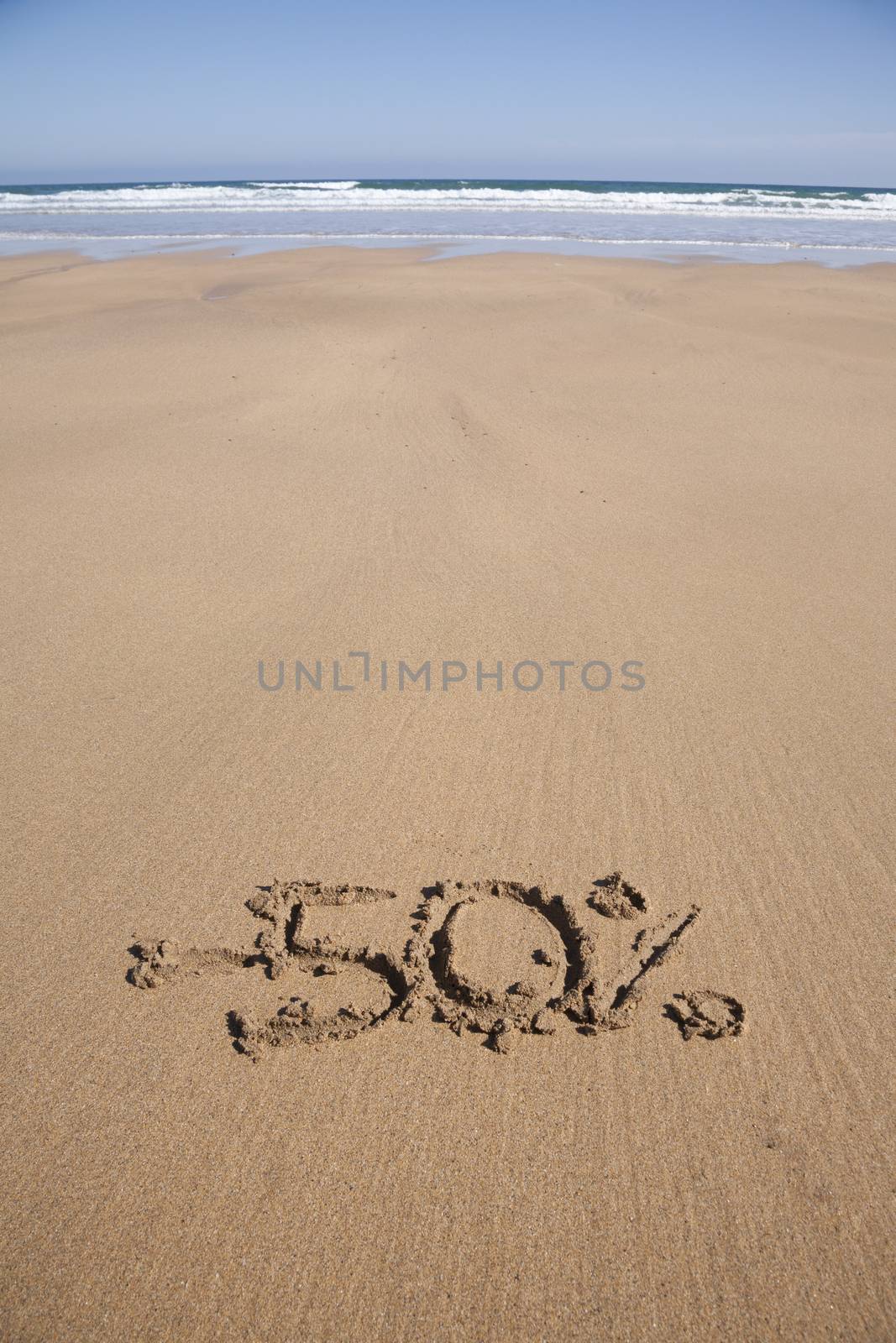 50 percent discount in earth text written on brown sand ground low tide beach ocean seashore in Spain Europe