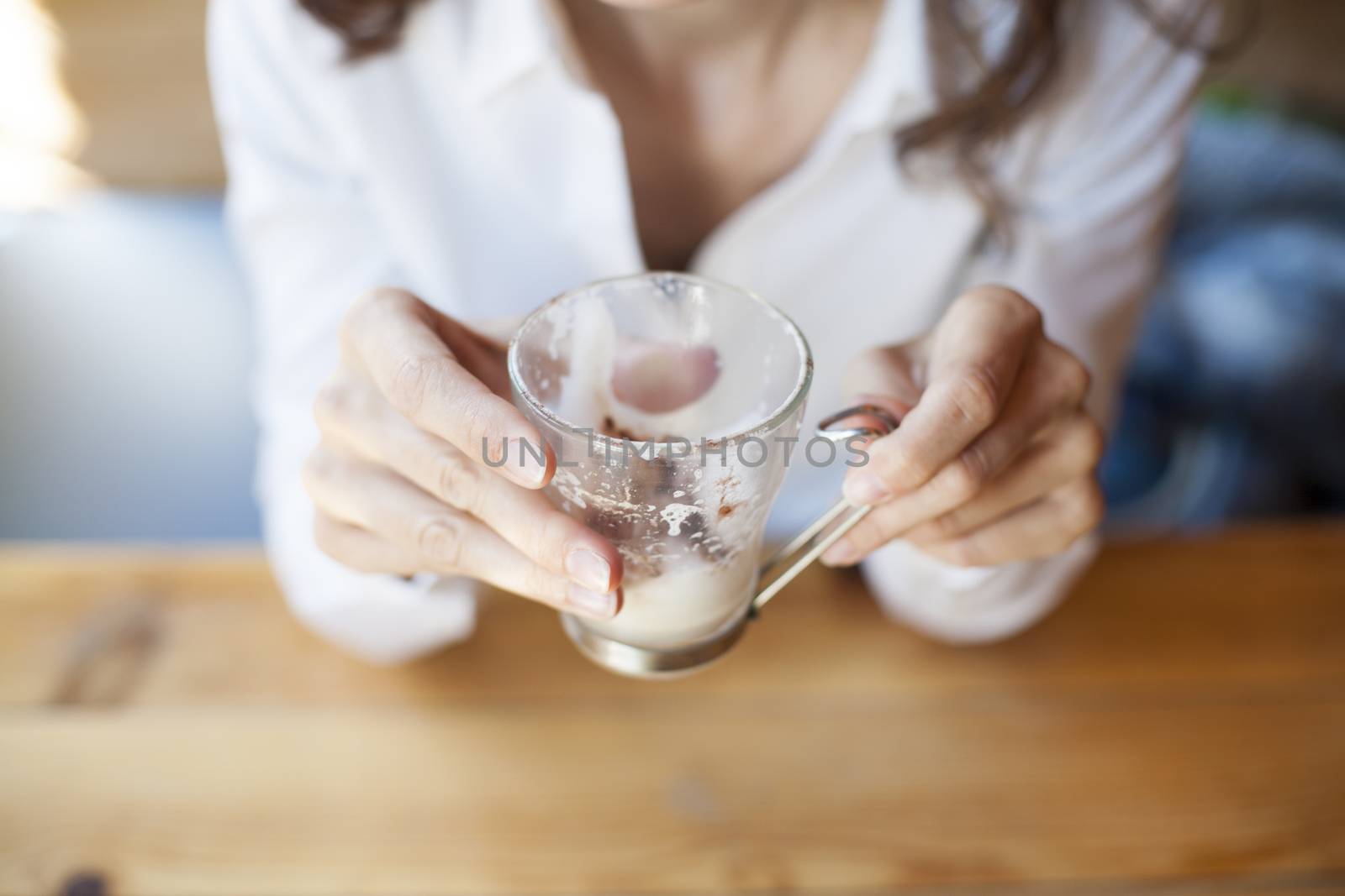 empty finished cappuccino coffee cup in hands of woman with white shirt on light brown wooden table cafe