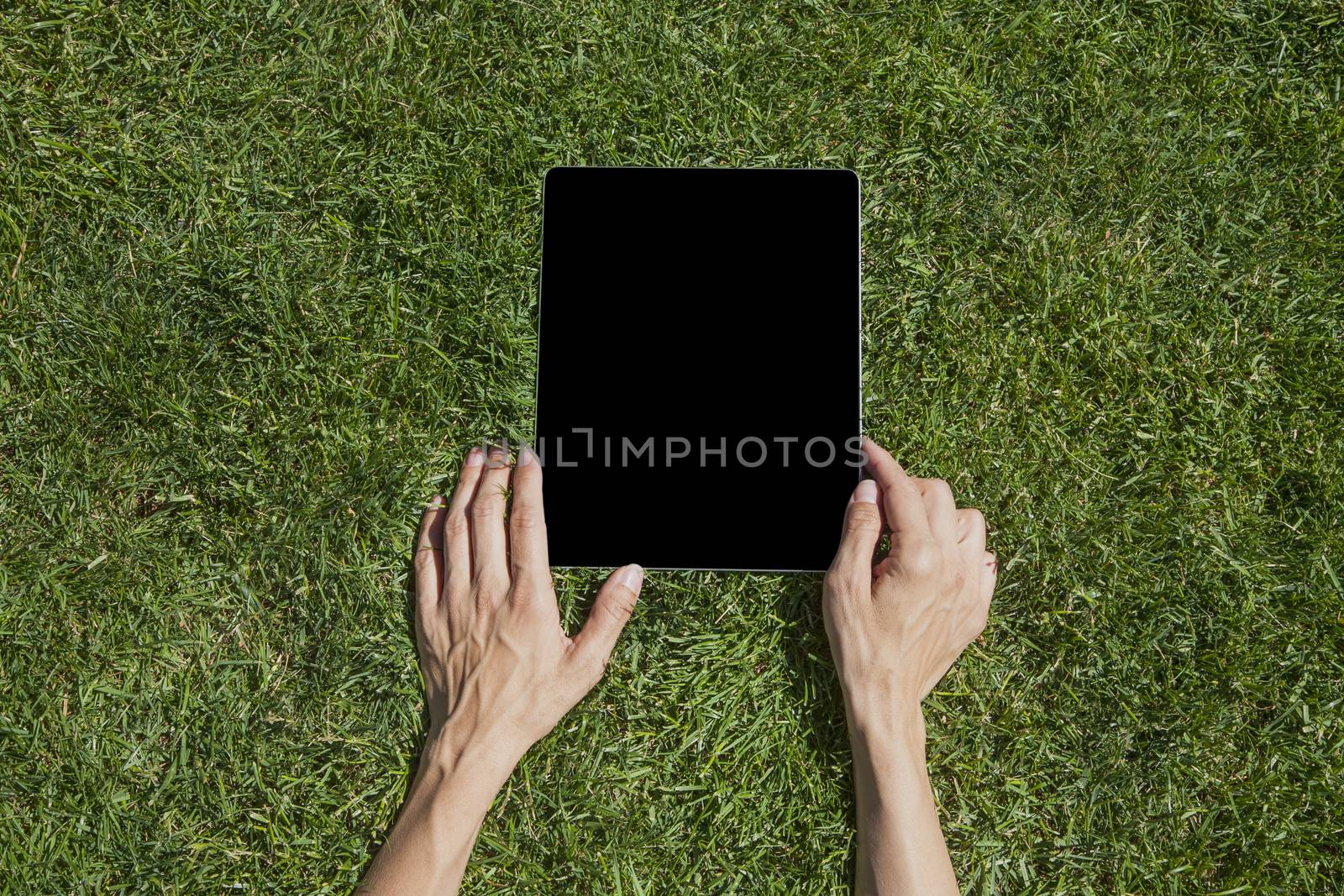 both hands of woman touching digital tablet blank black screen on green grass lawn in park