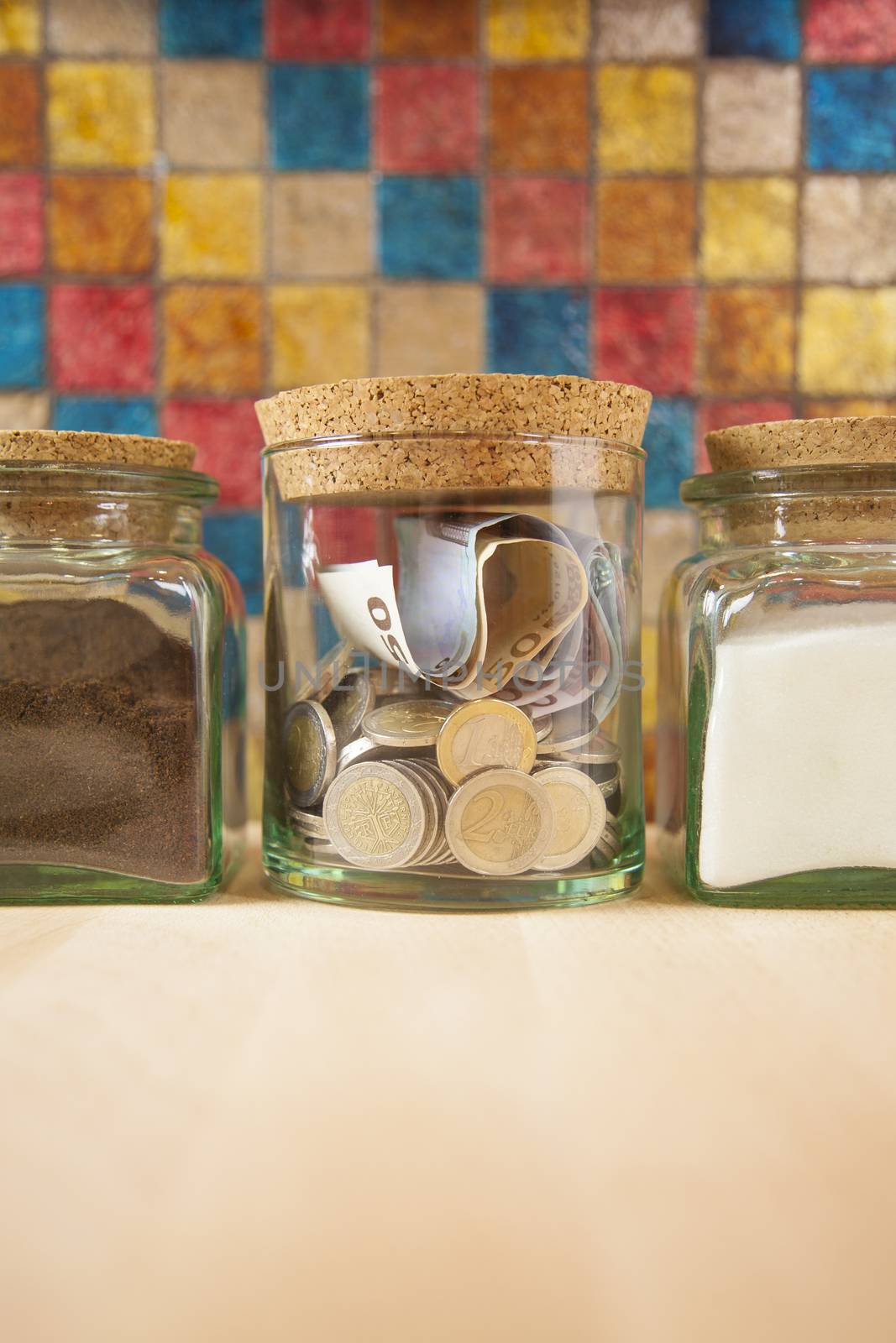 Euro coins and banknotes into crystal jar closed with cork plugs between coffee and white sugar on orange background