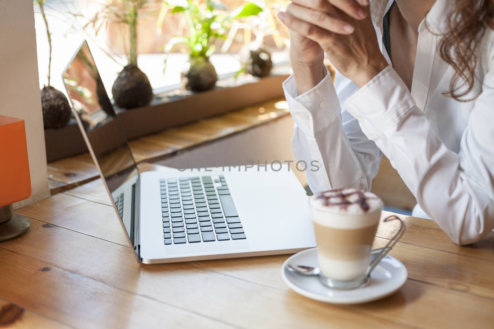 woman with white shirt in front of keyboard pc laptop and cappuccino coffee cup ready thinking on light brown wooden table