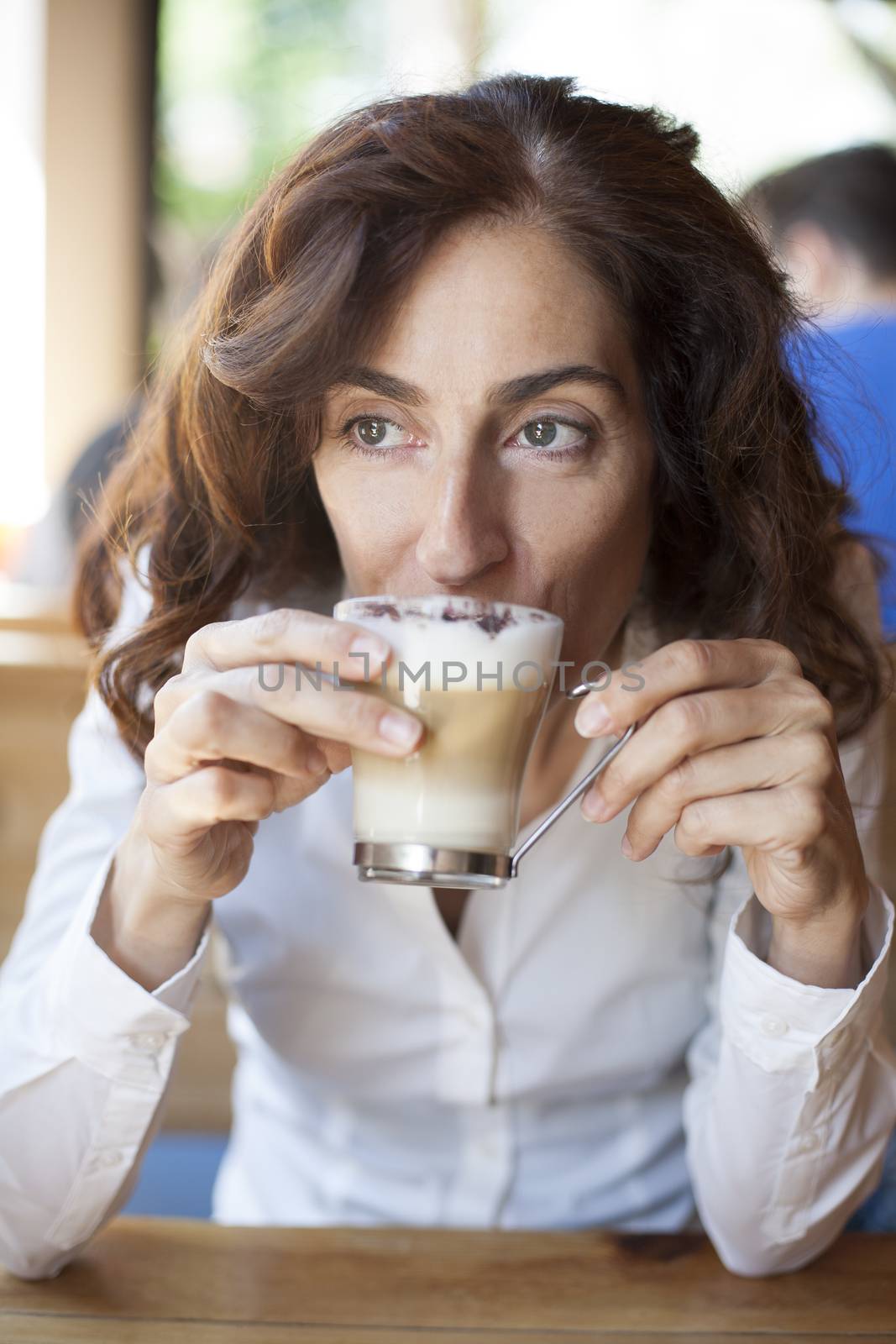 portrait of woman with white shirt drinking cappuccino coffee cup in hands on light brown wooden table cafe