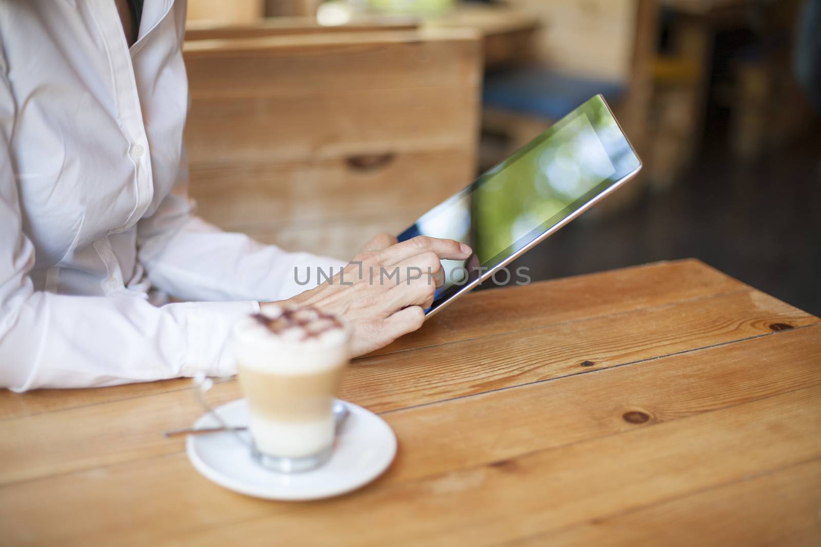 woman touching digital tablet blank screen with cappuccino coffee cup on light brown wooden table cafe