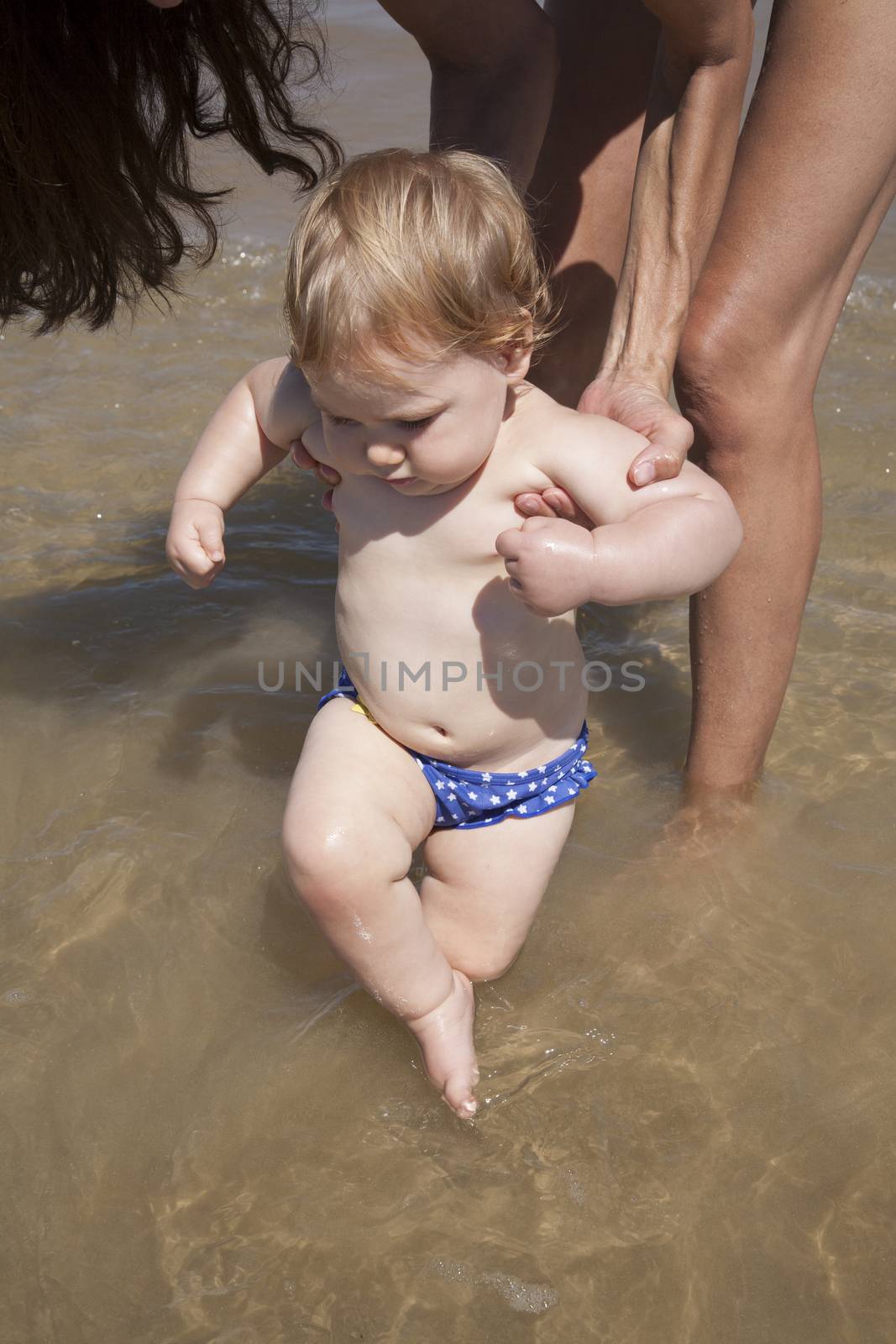 one year baby swimsuit touching water in woman mother hands at beach next to Conil Cadiz Spain