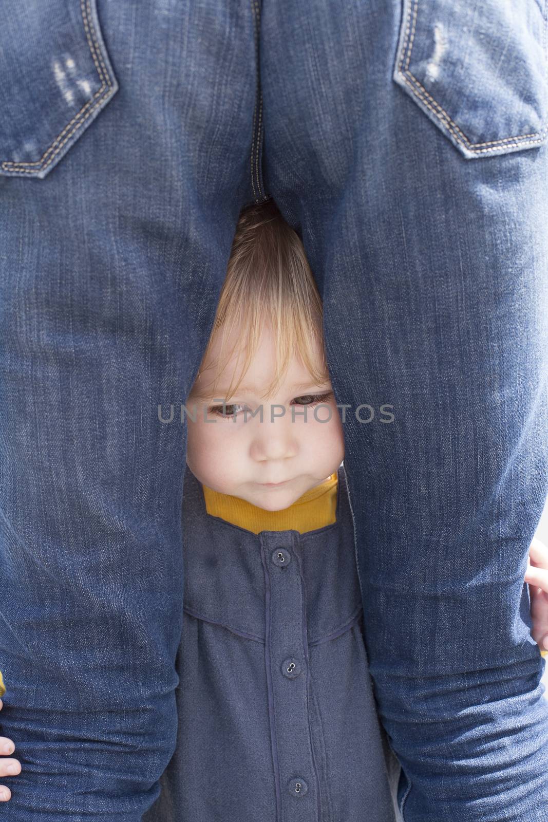 blonde nineteen month age baby with blue and yellow dress between mother blue jeans back woman legs