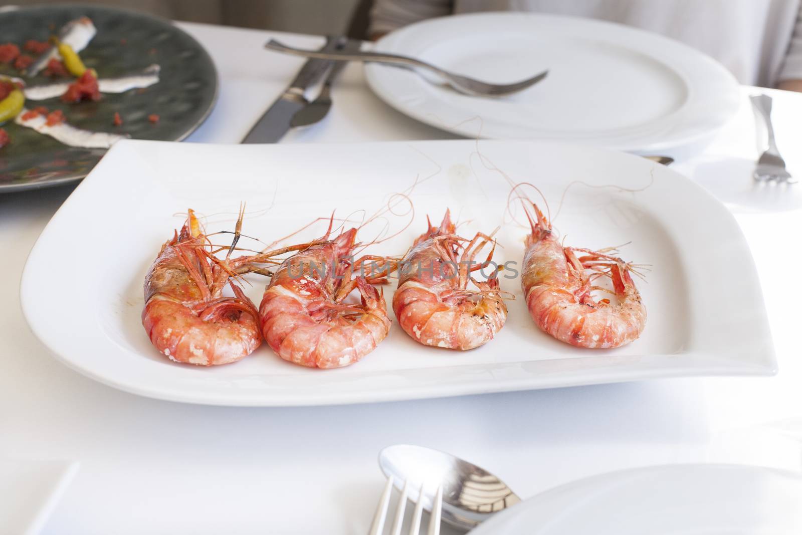 still life of white dish tray with four delicious big red grilled prawns on restaurant white table