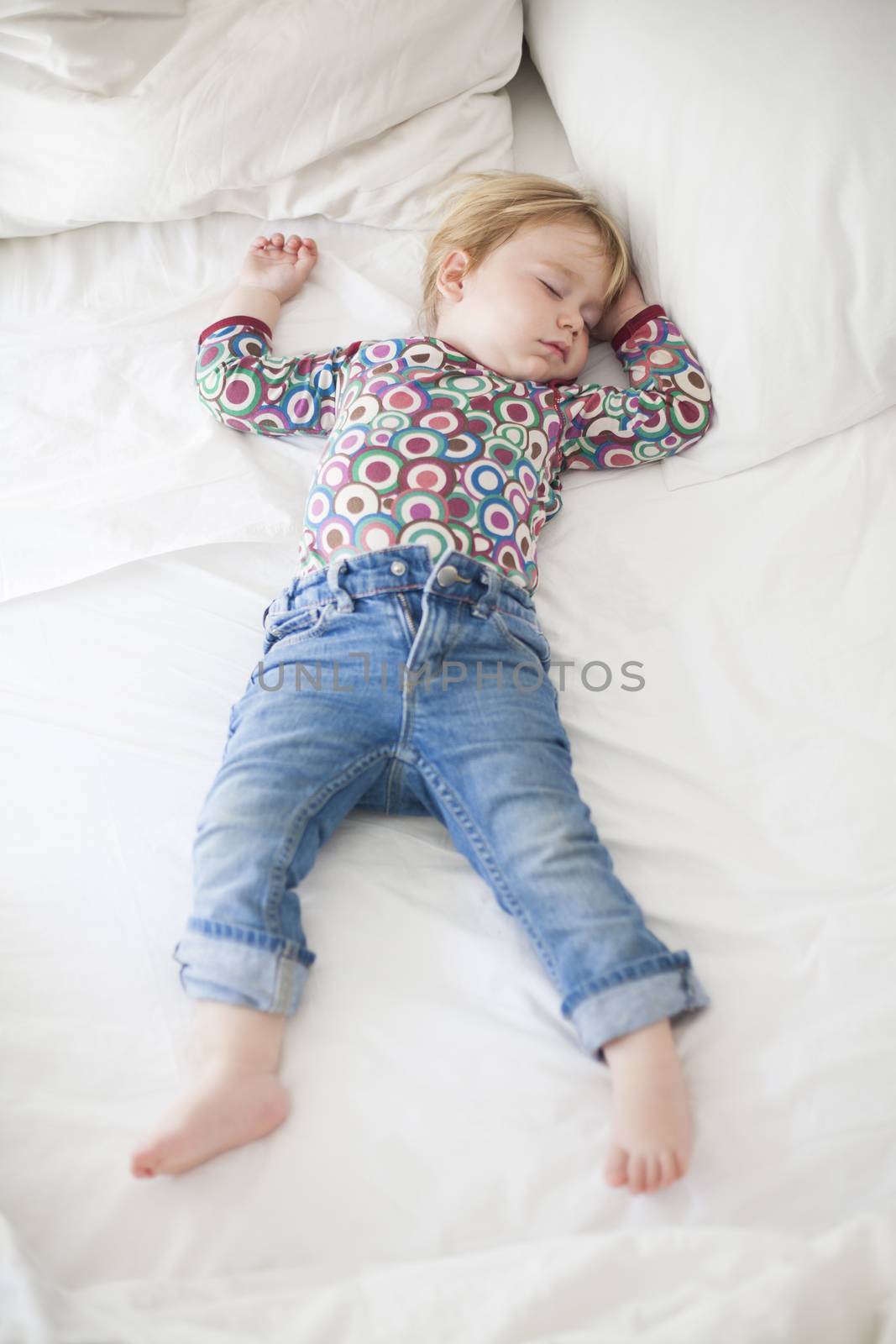 blonde caucasian baby face nineteen month age with colored shirt sleeping on white sheets king bed