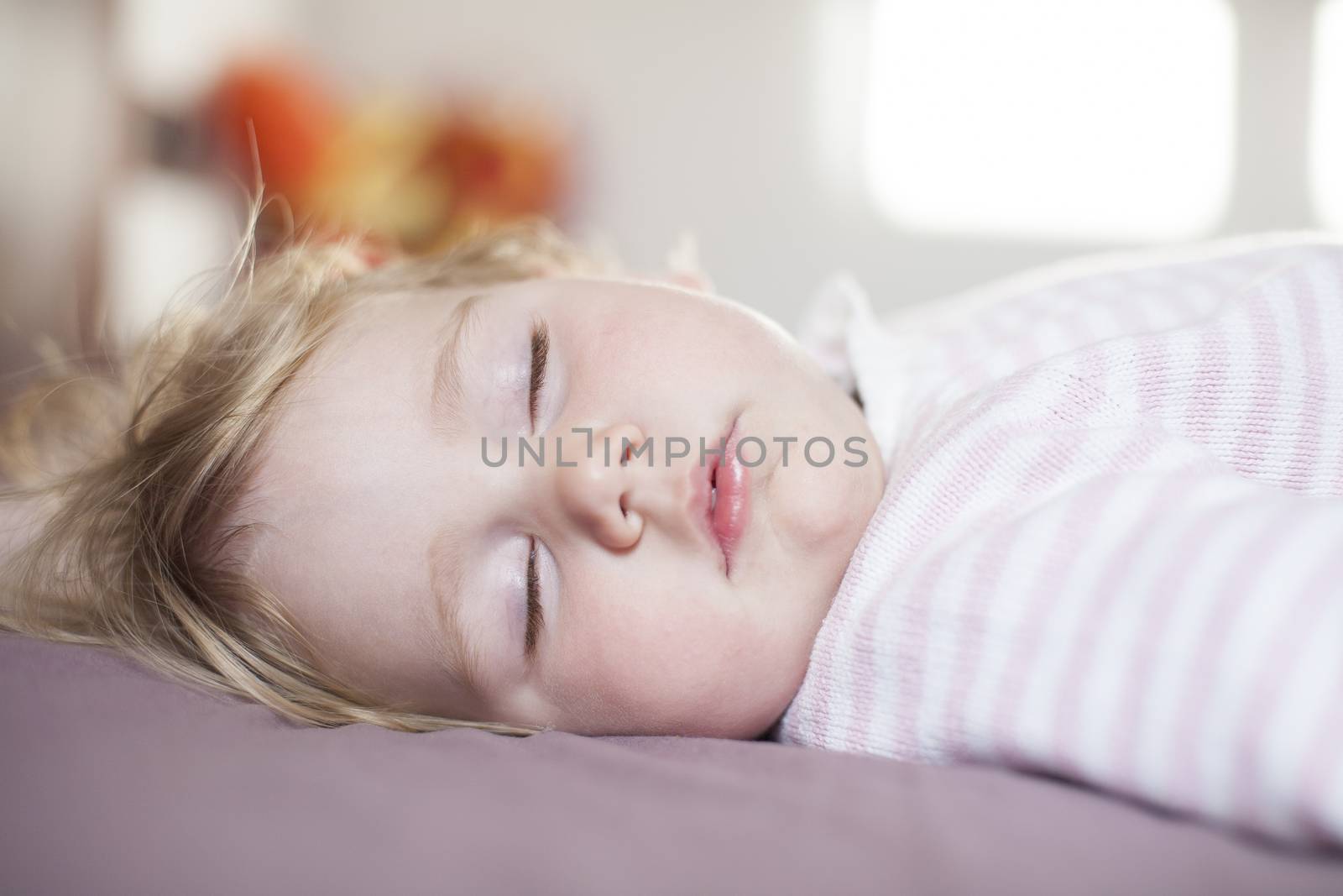 face of blonde caucasian baby nineteen month age with pink and white stripped jersey sleeping on brown sheets king bed