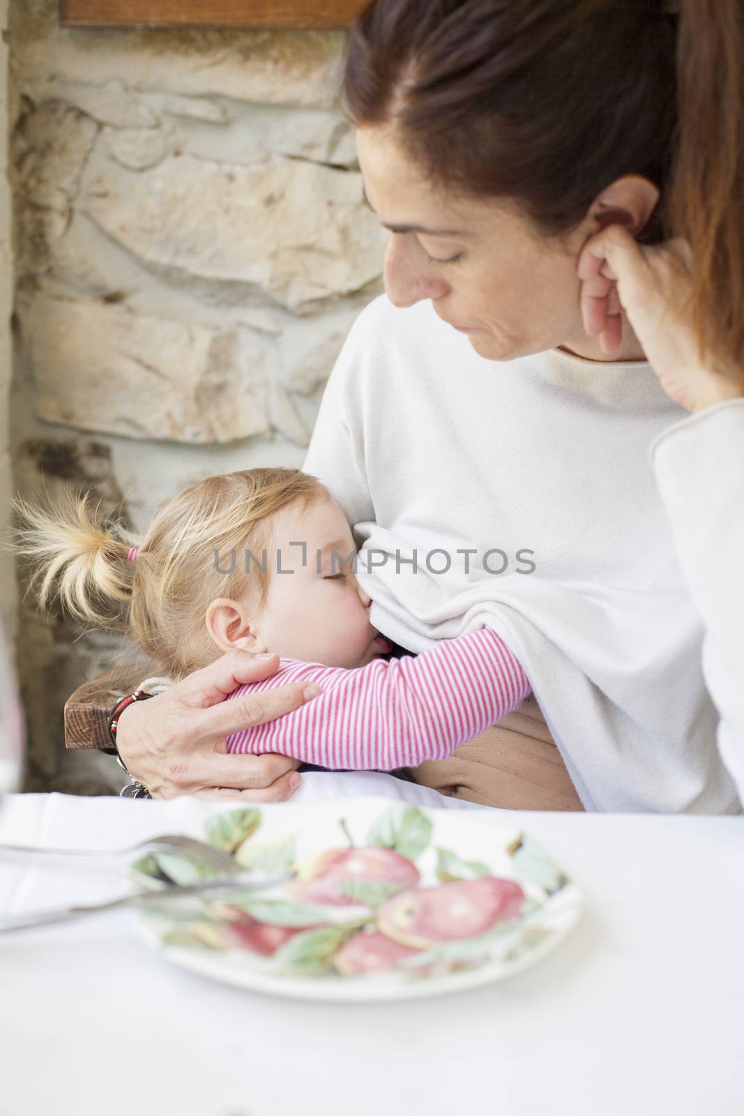 blonde two years age baby with pigtails breastfeeding woman mother white jersey sitting in restaurant table