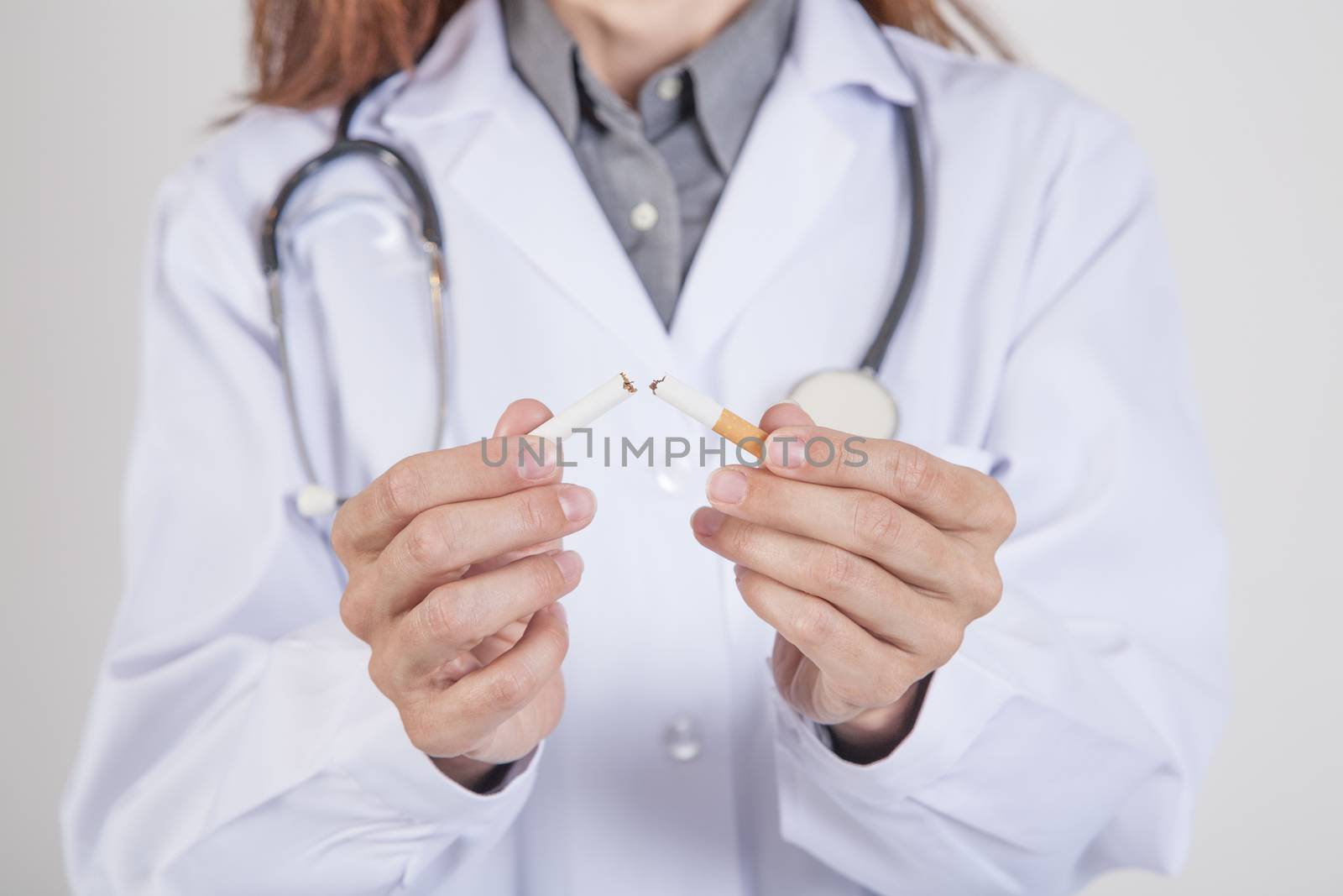 woman doctor with white gown and stethoscope breaking a cigarette tobacco in her hands over white background
