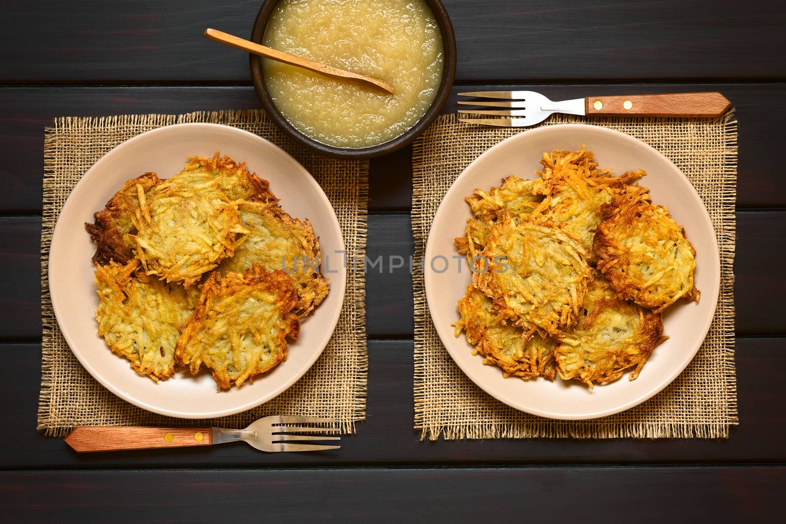 Homemade potato pancakes or fritters on plates with apple sauce, a traditional dish in Germany, photographed overhead on dark wood with natural light