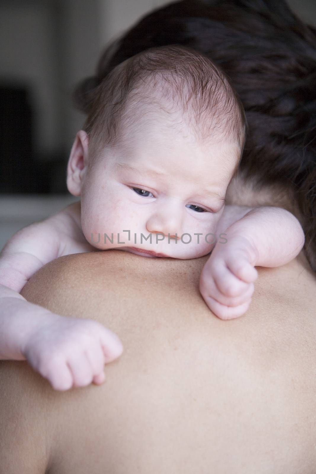portrait of twenty days age baby naked bare embraced open eyes looking with arms on shoulder of brunette woman mother cradling