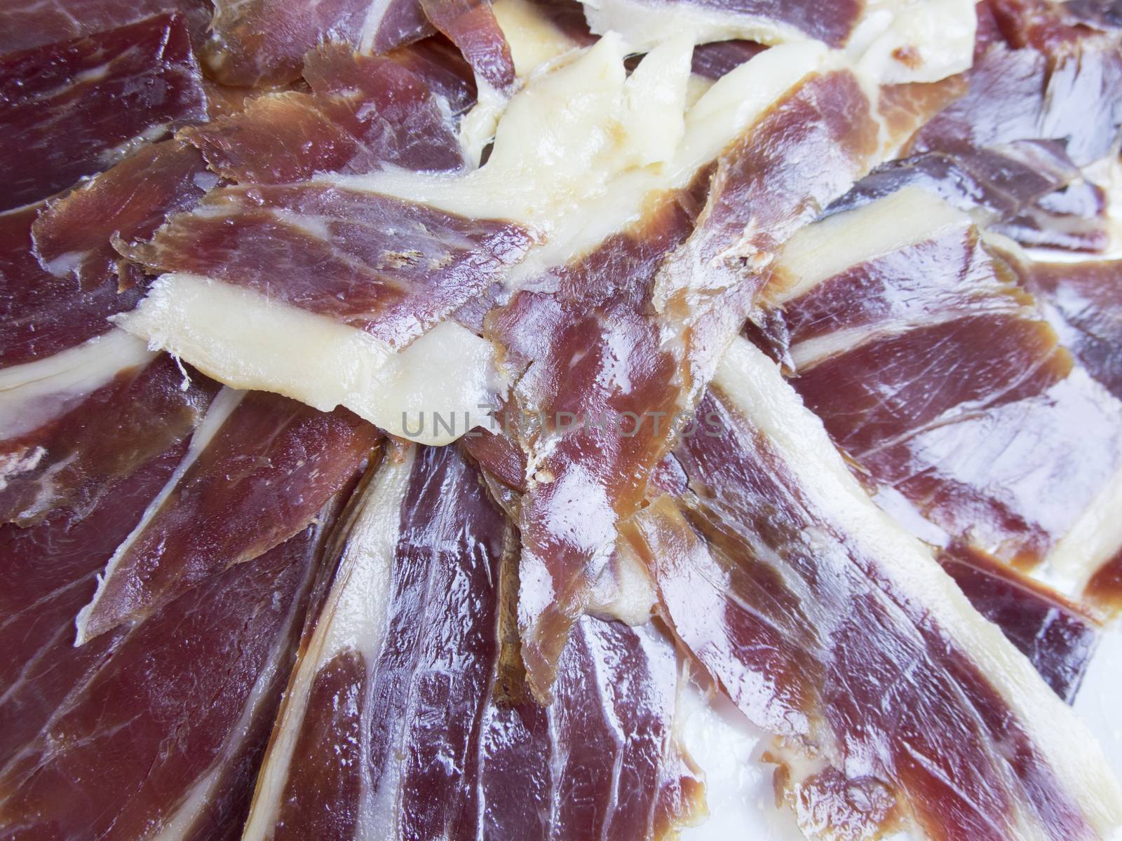 pile of typical spanish iberico ham sliced on white dish