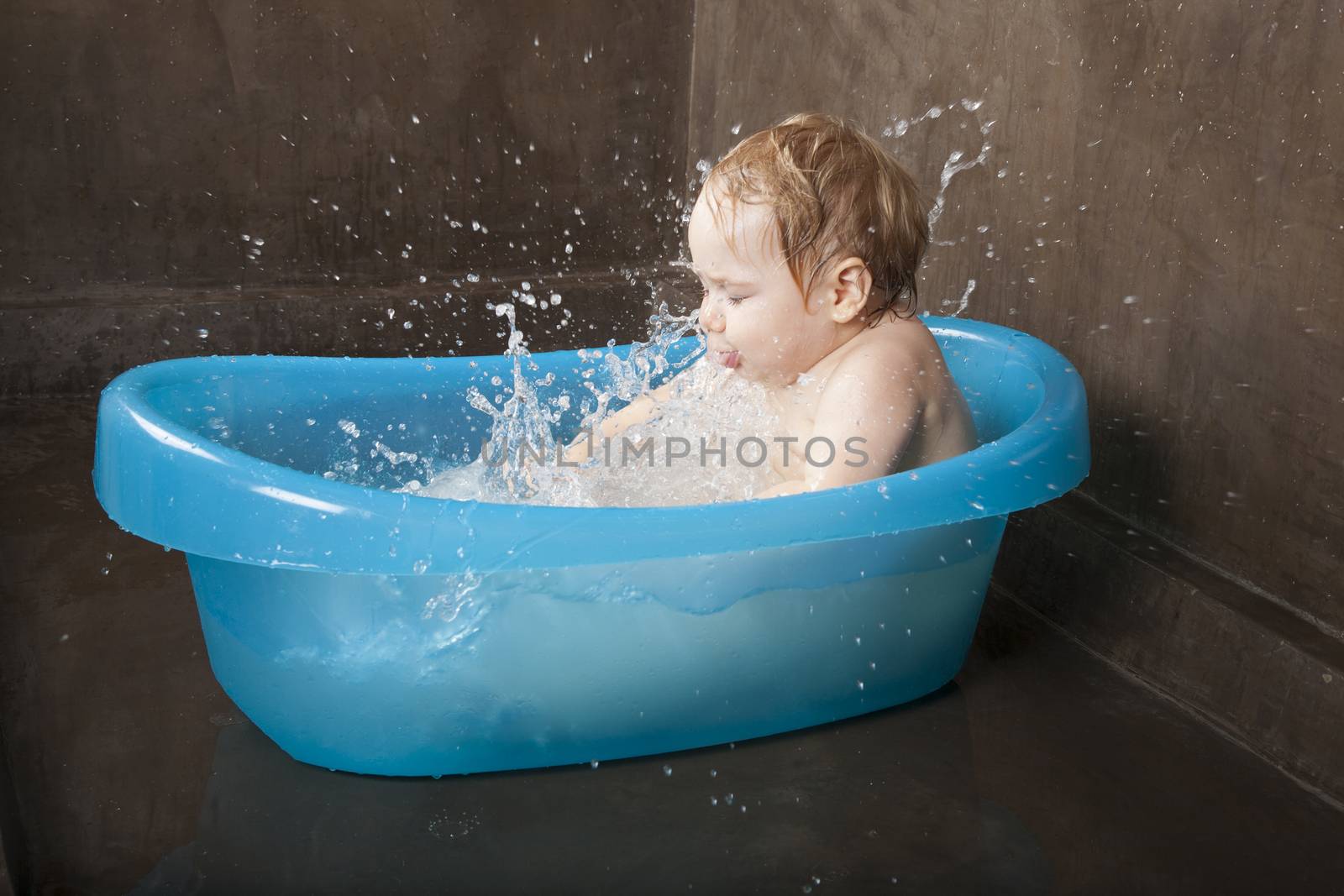 blonde naked baby washing in blue little bath indoor with brown background