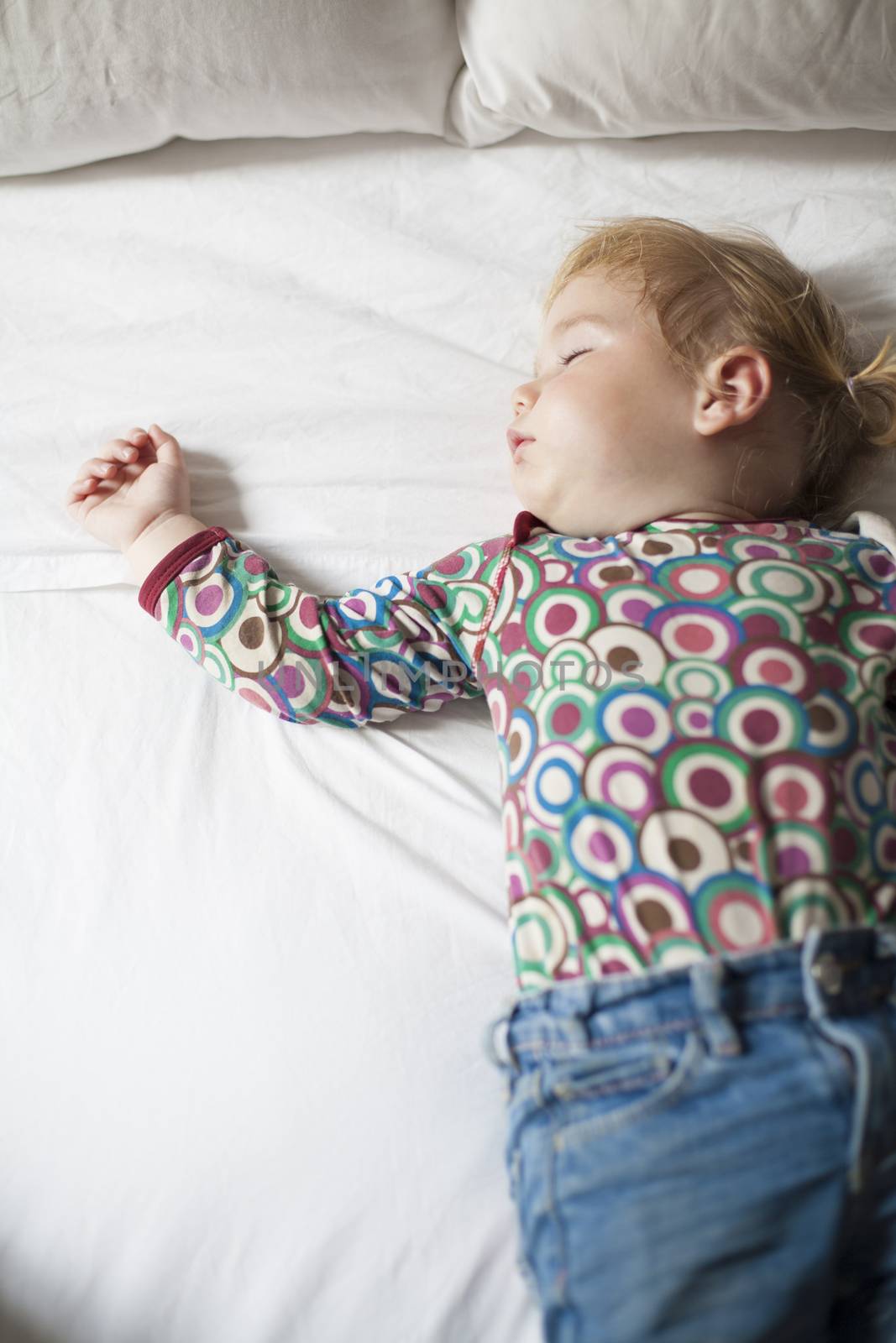 colored shirt baby sleeping on white bed by quintanilla