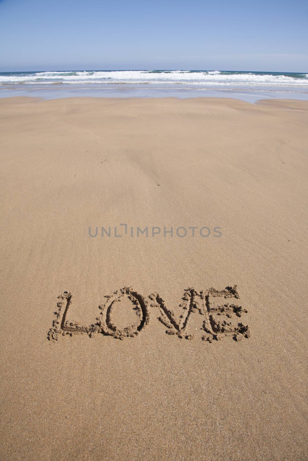 love word written on brown sand ground low tide beach ocean seashore in Spain Europe