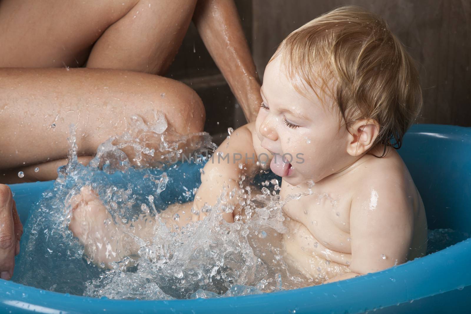 blonde naked baby washing in blue little bath indoor with brown background