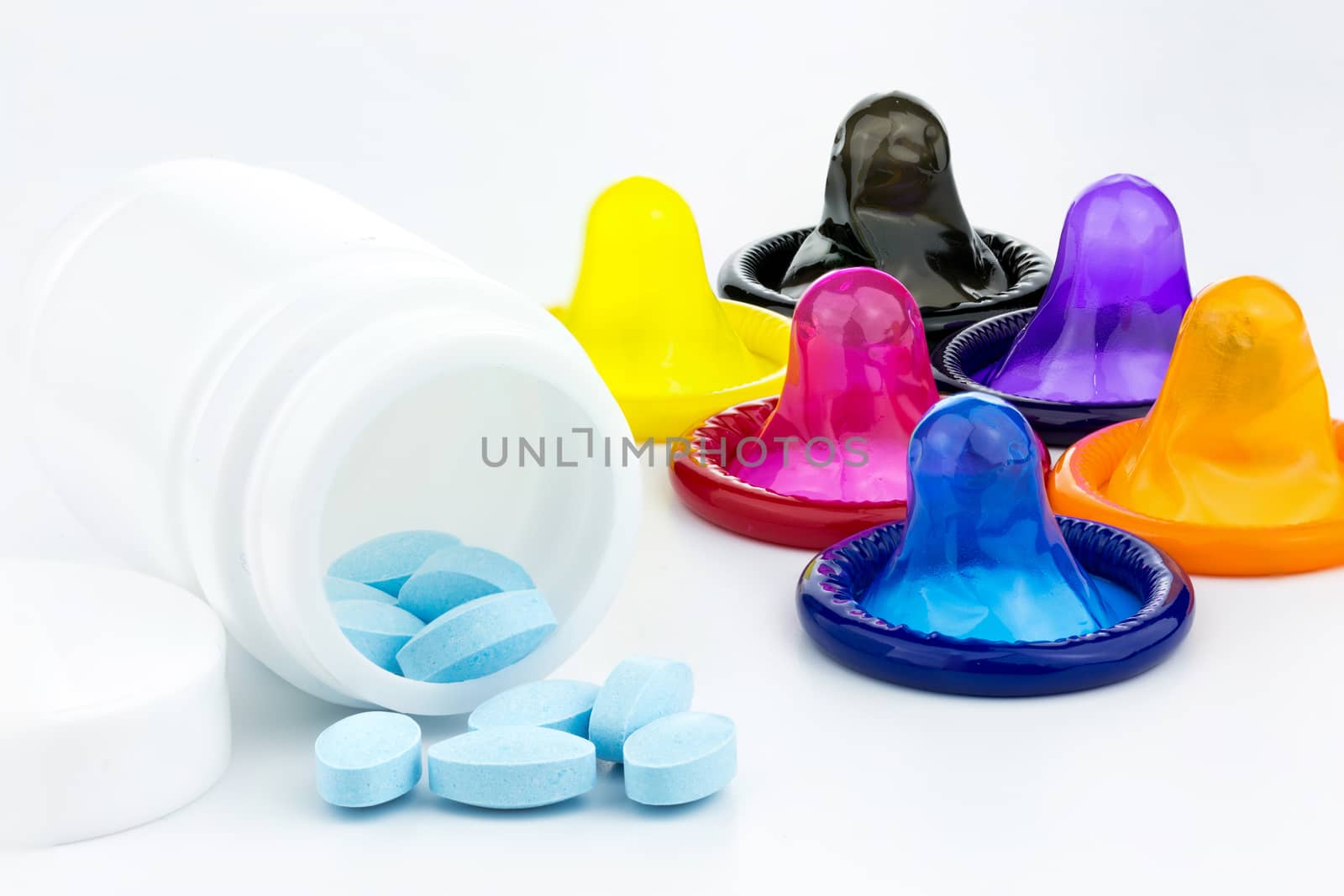 a pile of blue pills coming out of a bottle and a condom in the background (Isolated)
