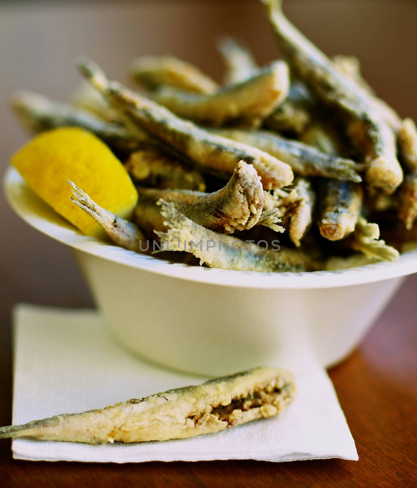 Delicious Deep Fried Small Fish in Bowl with Lemon. Focus on One Fish on Foreground